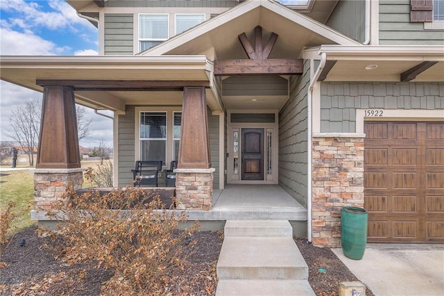 doorway to property featuring a porch, stone siding, and a garage