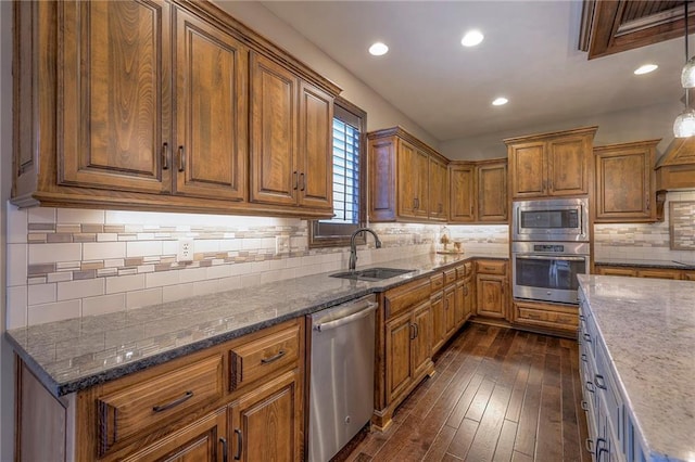 kitchen with appliances with stainless steel finishes, brown cabinetry, a sink, and dark stone counters