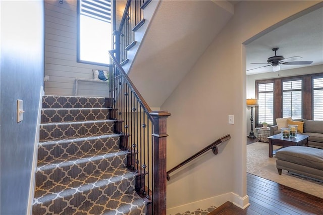 stairway featuring wood-type flooring, ceiling fan, and baseboards