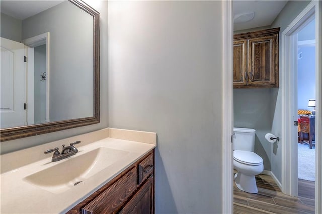 bathroom with baseboards, vanity, toilet, and wood finished floors