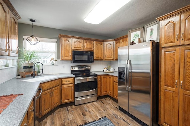 kitchen with backsplash, appliances with stainless steel finishes, wood finished floors, brown cabinetry, and a sink