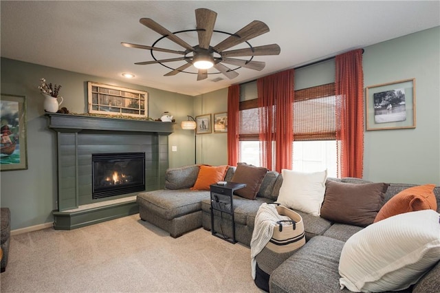 living room featuring a glass covered fireplace, baseboards, carpet floors, and ceiling fan