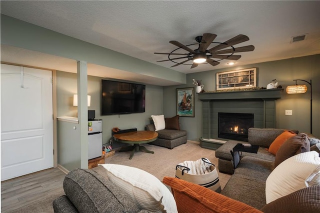 living room featuring ceiling fan, visible vents, a textured ceiling, and a glass covered fireplace