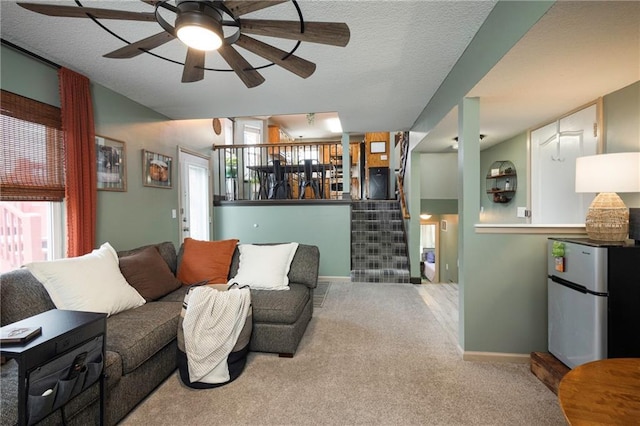 living room featuring a textured ceiling, carpet flooring, baseboards, ceiling fan, and stairs