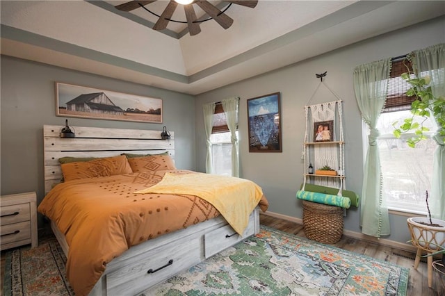 bedroom featuring ceiling fan, baseboards, multiple windows, and wood finished floors