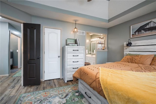 bedroom featuring connected bathroom, visible vents, baseboards, and wood finished floors