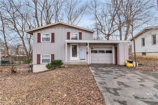 tri-level home featuring a garage, fence, board and batten siding, and aphalt driveway