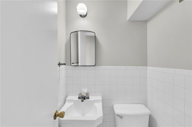 half bathroom featuring toilet, tile walls, and a sink