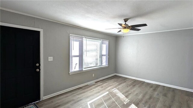 foyer entrance featuring ornamental molding, a textured ceiling, baseboards, and wood finished floors