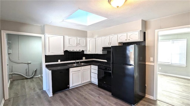 kitchen with a skylight, dark countertops, white cabinetry, a sink, and black appliances