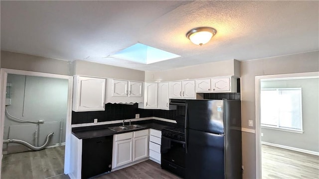 kitchen with a skylight, dark countertops, white cabinets, a sink, and black appliances