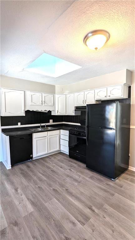 kitchen featuring dark countertops, light wood-style flooring, white cabinetry, a textured ceiling, and black appliances