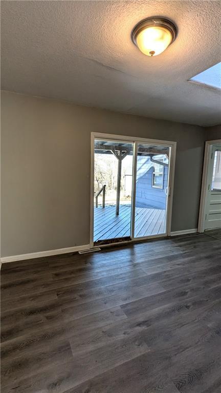 unfurnished room featuring a textured ceiling, dark wood-type flooring, a wealth of natural light, and baseboards