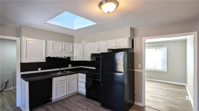 kitchen with a skylight, a sink, white cabinetry, black appliances, and dark countertops