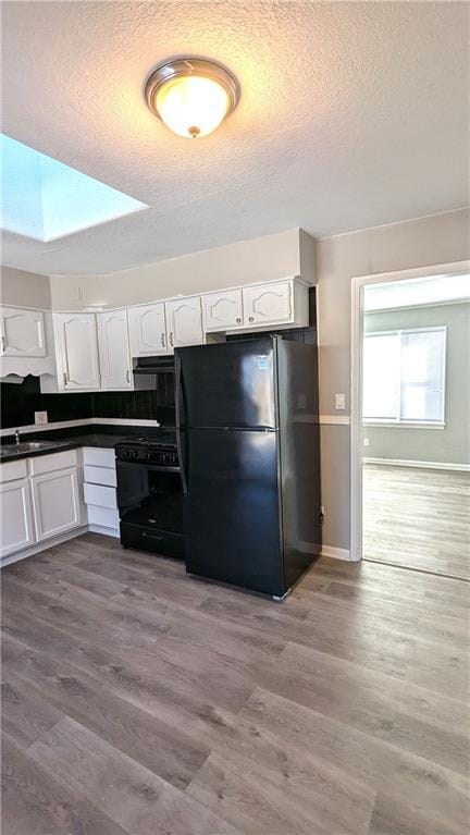 kitchen with dark countertops, white cabinets, light wood-style flooring, and black appliances