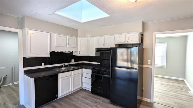 kitchen featuring a skylight, dark countertops, white cabinetry, a sink, and black appliances