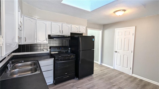 kitchen featuring dark countertops, white cabinets, a sink, under cabinet range hood, and black appliances