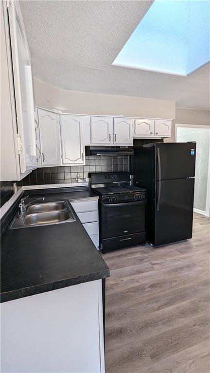 kitchen featuring dark countertops, under cabinet range hood, black appliances, white cabinetry, and a sink