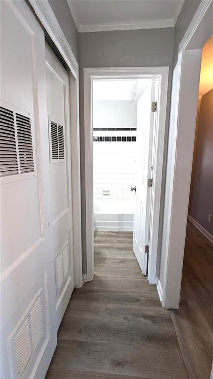 corridor featuring ornamental molding, wood finished floors, visible vents, and baseboards