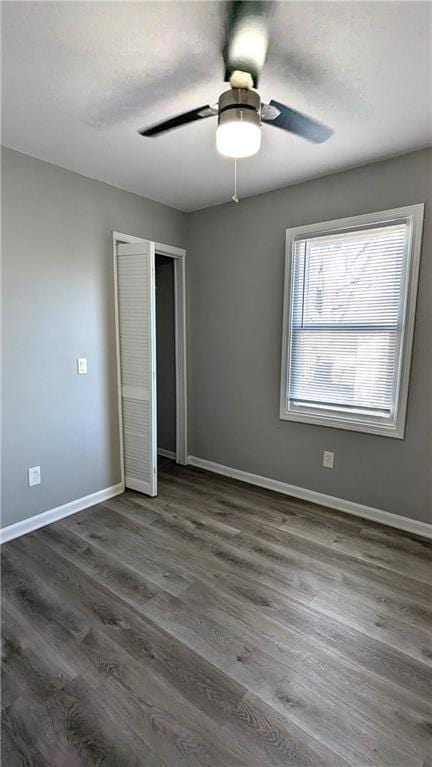 unfurnished bedroom featuring dark wood-style floors, a closet, baseboards, and a ceiling fan