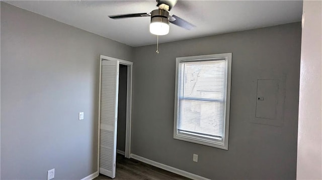 empty room featuring ceiling fan, electric panel, baseboards, and dark wood-style flooring