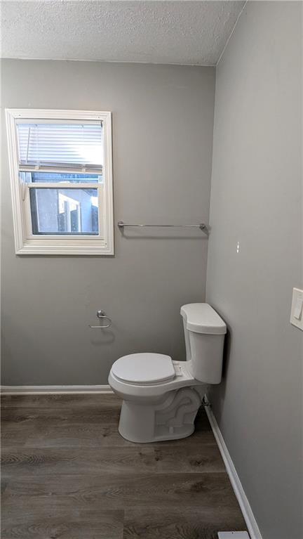 bathroom with a textured ceiling, wood finished floors, toilet, and baseboards