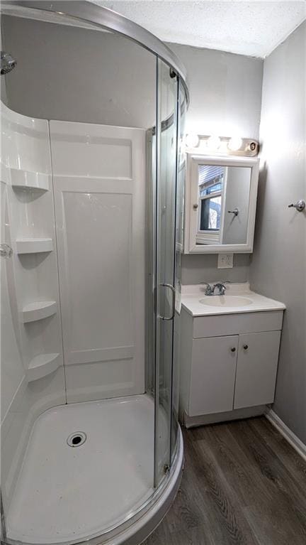 bathroom with a textured ceiling, wood finished floors, a shower stall, and vanity