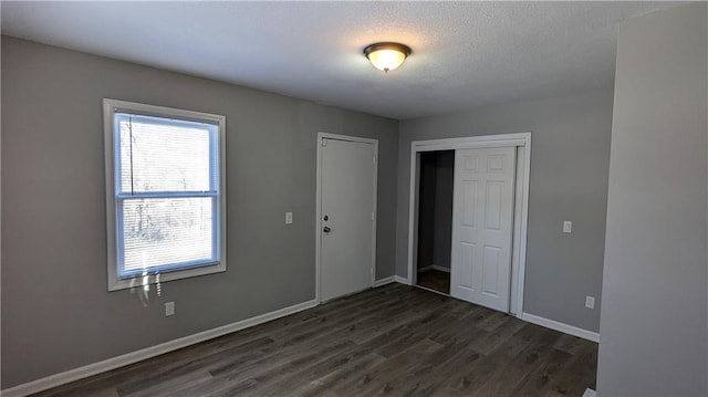 unfurnished room with dark wood-style flooring, a textured ceiling, and baseboards