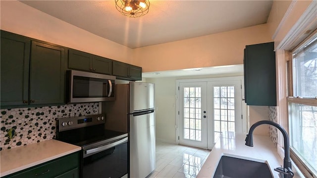 kitchen with a sink, french doors, appliances with stainless steel finishes, decorative backsplash, and green cabinetry