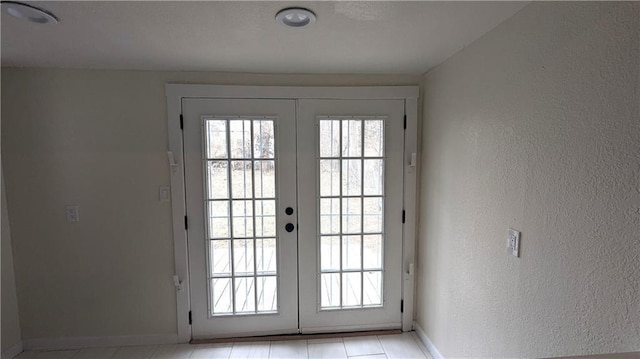 doorway to outside featuring a textured wall, french doors, and baseboards