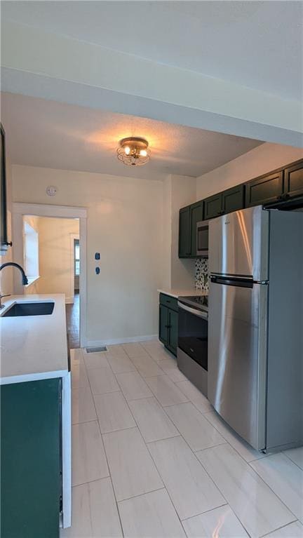 kitchen with baseboards, appliances with stainless steel finishes, a sink, light countertops, and backsplash