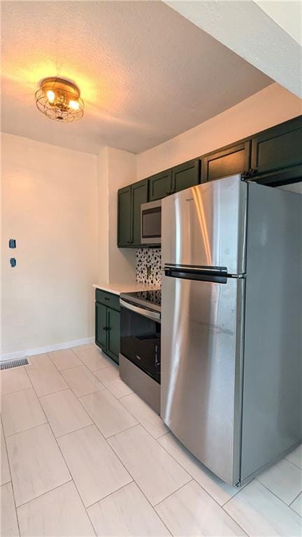 kitchen with green cabinets, appliances with stainless steel finishes, a textured ceiling, and visible vents