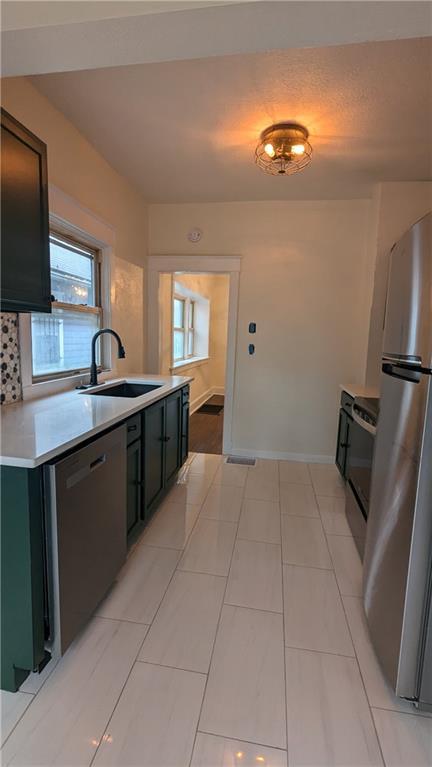 kitchen featuring tasteful backsplash, baseboards, stainless steel appliances, light countertops, and a sink