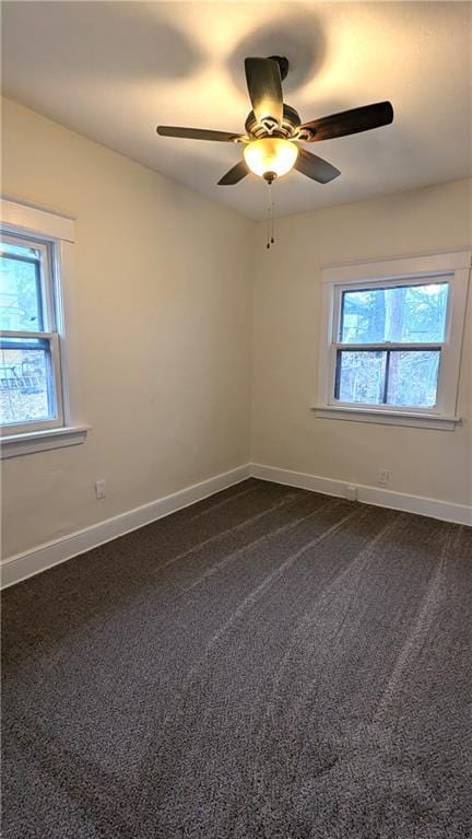 empty room with dark carpet, a ceiling fan, and baseboards