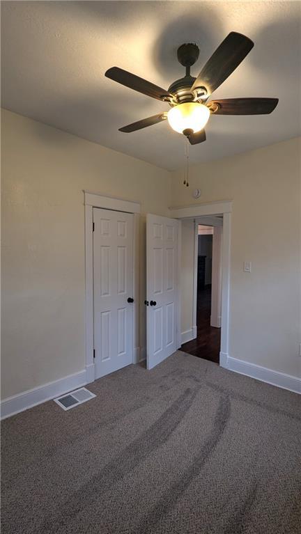 empty room featuring ceiling fan, baseboards, visible vents, and dark carpet