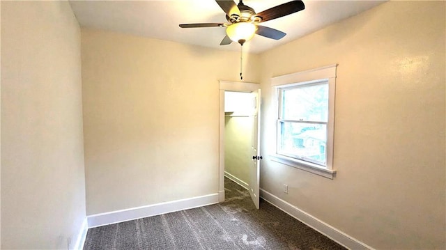 spare room featuring baseboards, dark carpet, and a ceiling fan