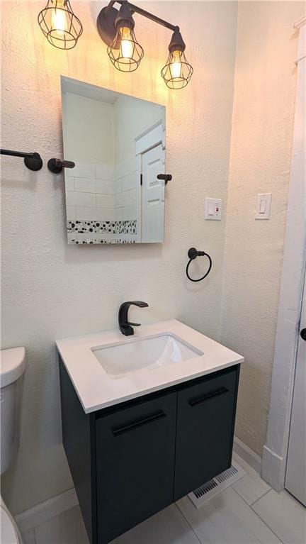 bathroom with visible vents, a textured wall, vanity, and toilet