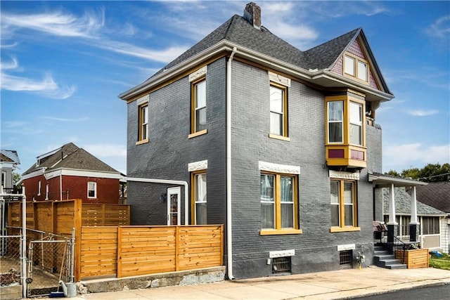 view of front of house featuring brick siding, fence, a chimney, and roof with shingles