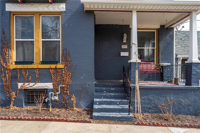 entrance to property with a porch and brick siding