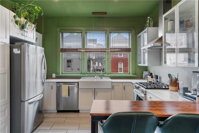 kitchen with stainless steel appliances, a sink, white cabinetry, wall chimney range hood, and backsplash