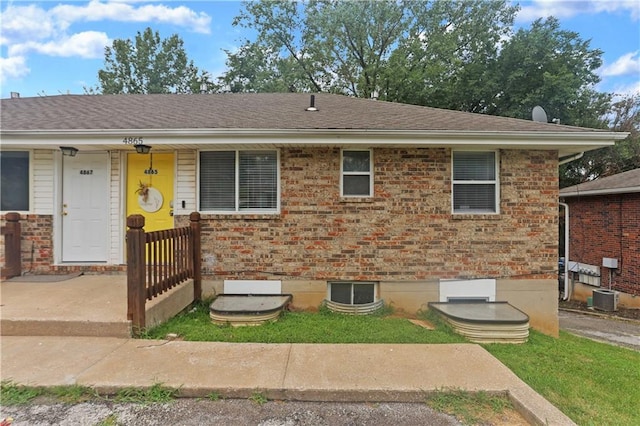 view of front of property featuring cooling unit, brick siding, and roof with shingles