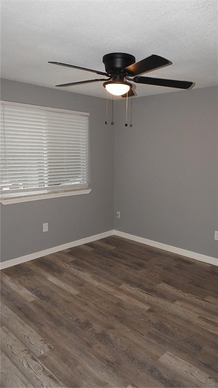 spare room featuring a ceiling fan, dark wood-style floors, baseboards, and a textured ceiling