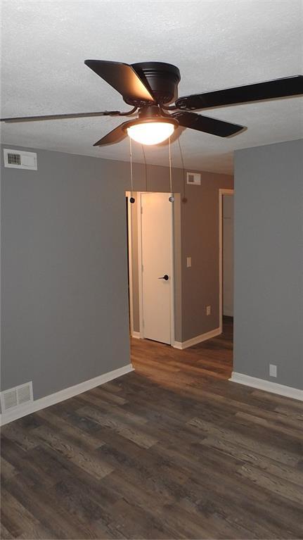 empty room with dark wood-type flooring, visible vents, and a textured ceiling