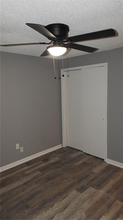 empty room featuring baseboards, a ceiling fan, dark wood-style flooring, and a textured ceiling