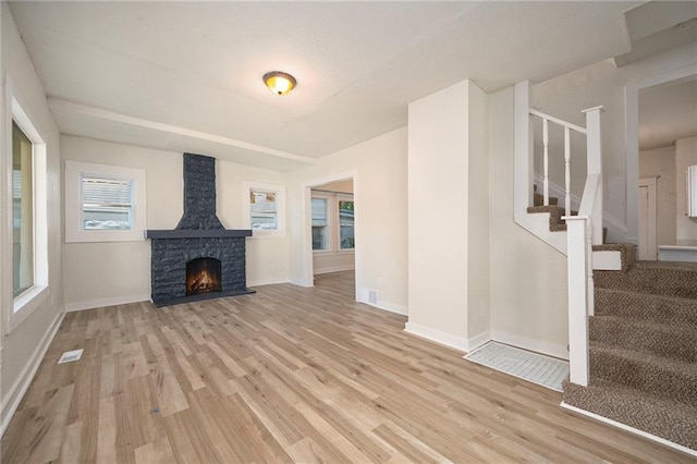 unfurnished living room featuring stairway, light wood-type flooring, a fireplace, and baseboards