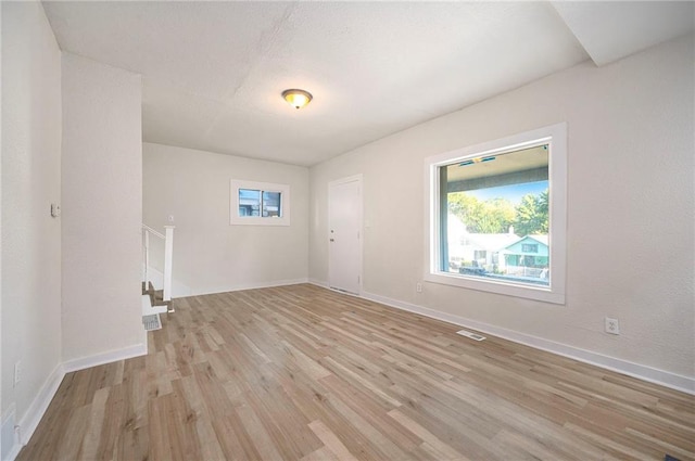 unfurnished room featuring light wood-type flooring, visible vents, baseboards, and stairs