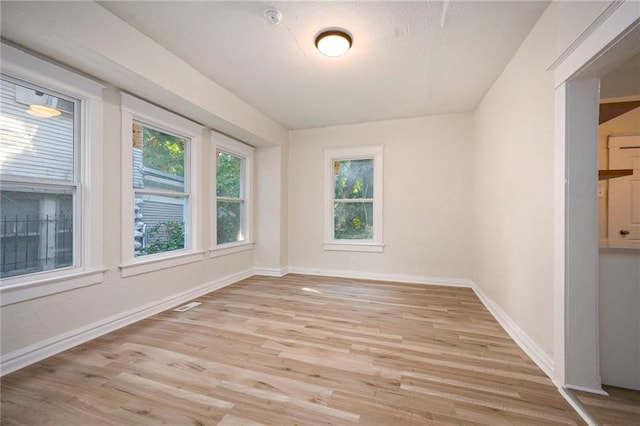 empty room with light wood-style floors, visible vents, a textured ceiling, and baseboards