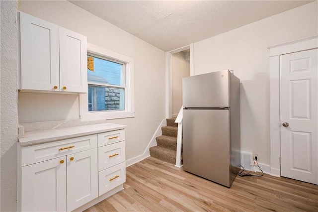 kitchen featuring baseboards, light wood-style flooring, freestanding refrigerator, and white cabinets