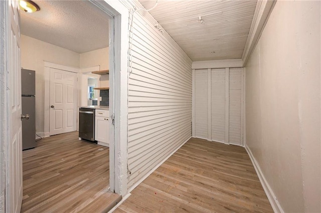 corridor with baseboards, a textured ceiling, and light wood finished floors