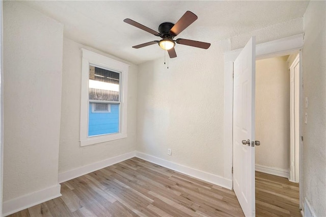 spare room featuring light wood-style flooring, baseboards, ceiling fan, and a textured wall